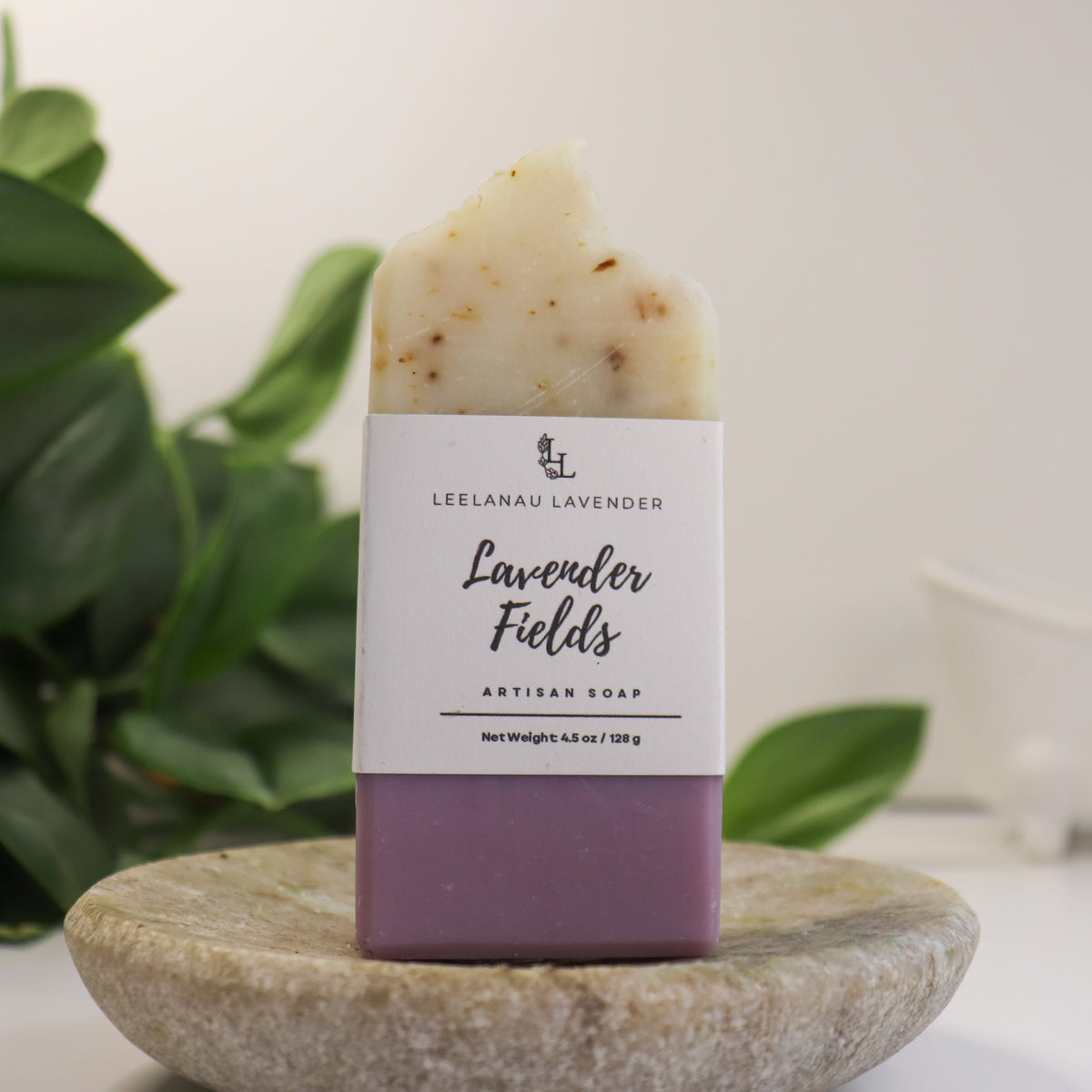 Bar of soap labeled 'Lavender Fields' by Leelanau Lavender on a stone surface with green leaves in the background.